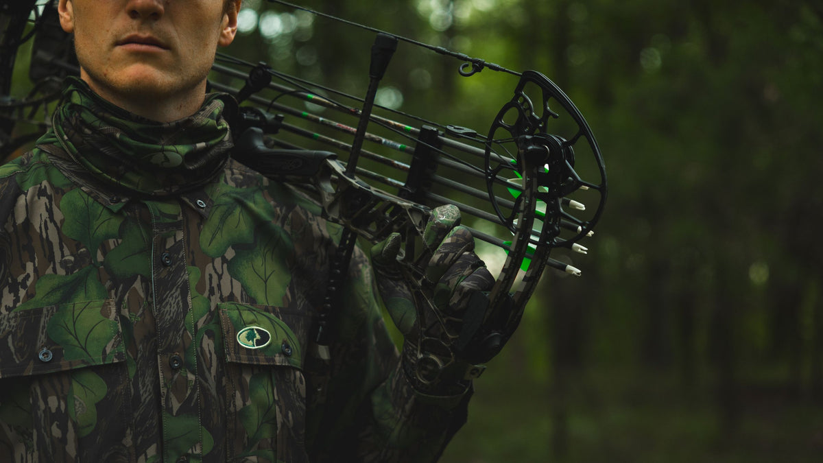 Hunter in camouflage holding a compound bow in a forest